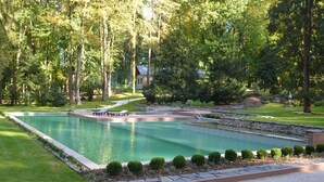 A rectangular swimming pool with a stone border, surrounded by well-maintained grass and small bushes.