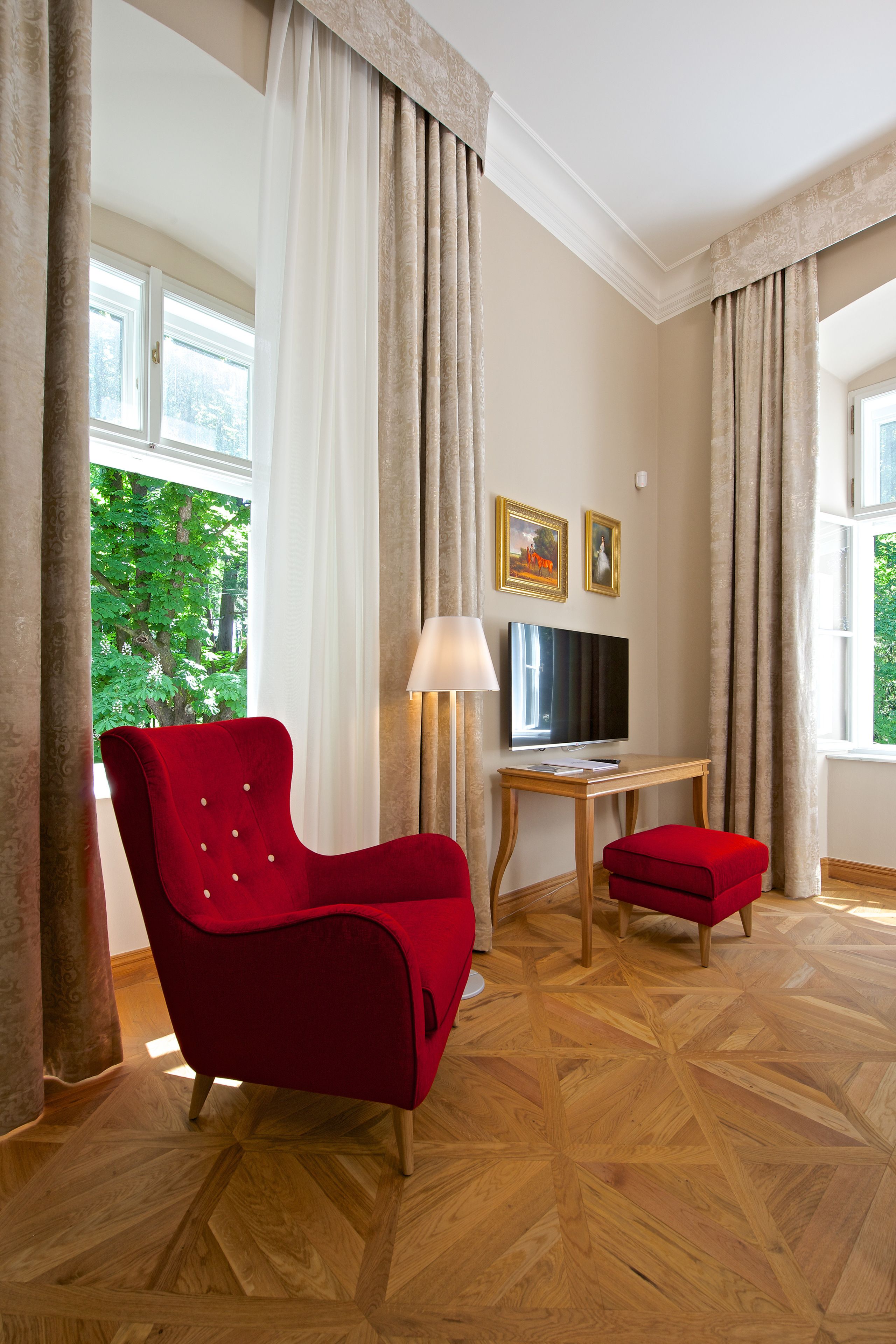 A room with a red chair, a wooden table, a TV, and a lamp.