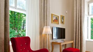 A room with a red chair, a wooden table, a TV, and a lamp.