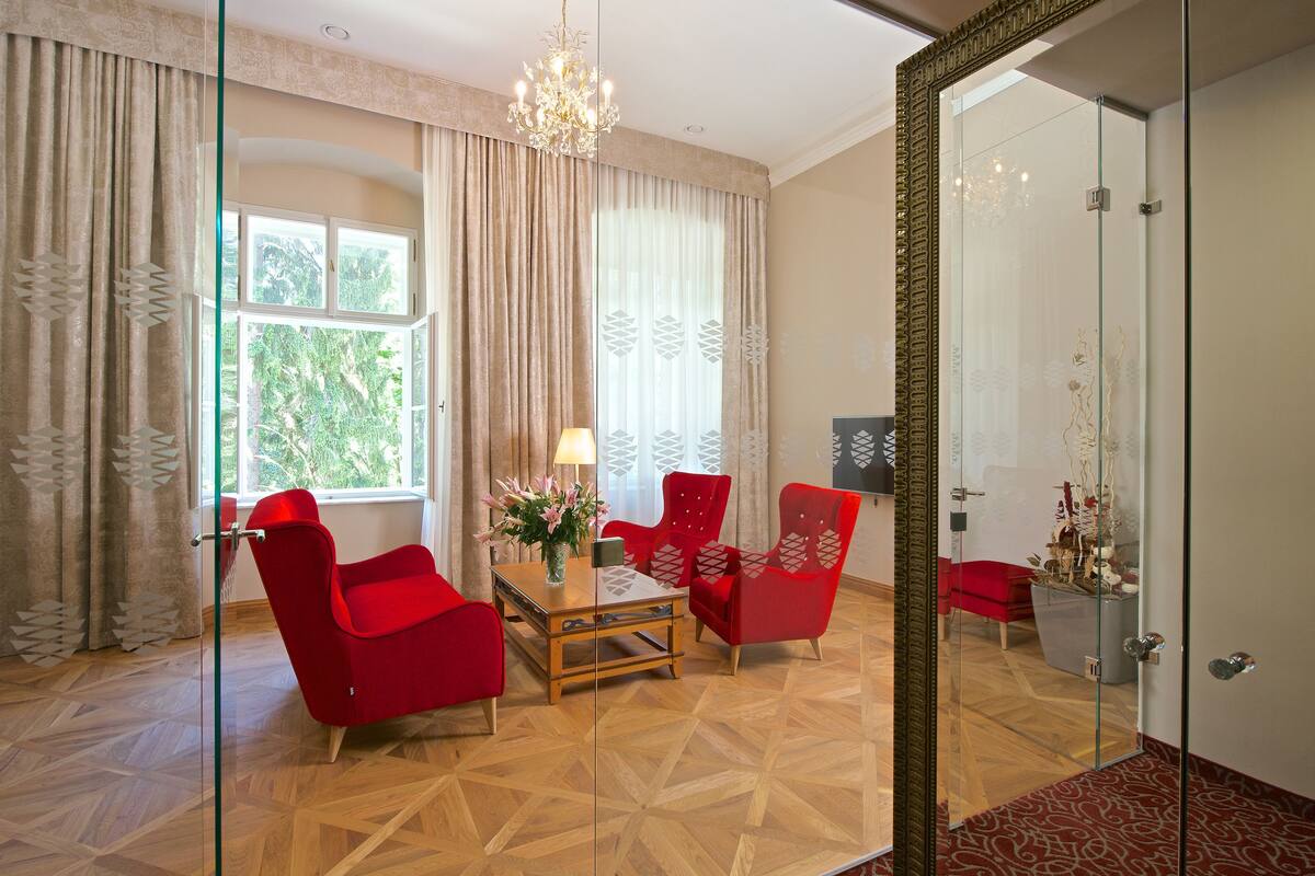A modern room with a wooden parquet floor, a glass partition, red armchairs, a wooden coffee table, and a chandelier.