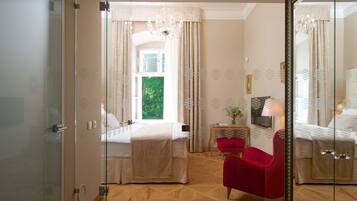 A hotel room with a bed, a red chair, a small table with a lamp, and a large mirror.