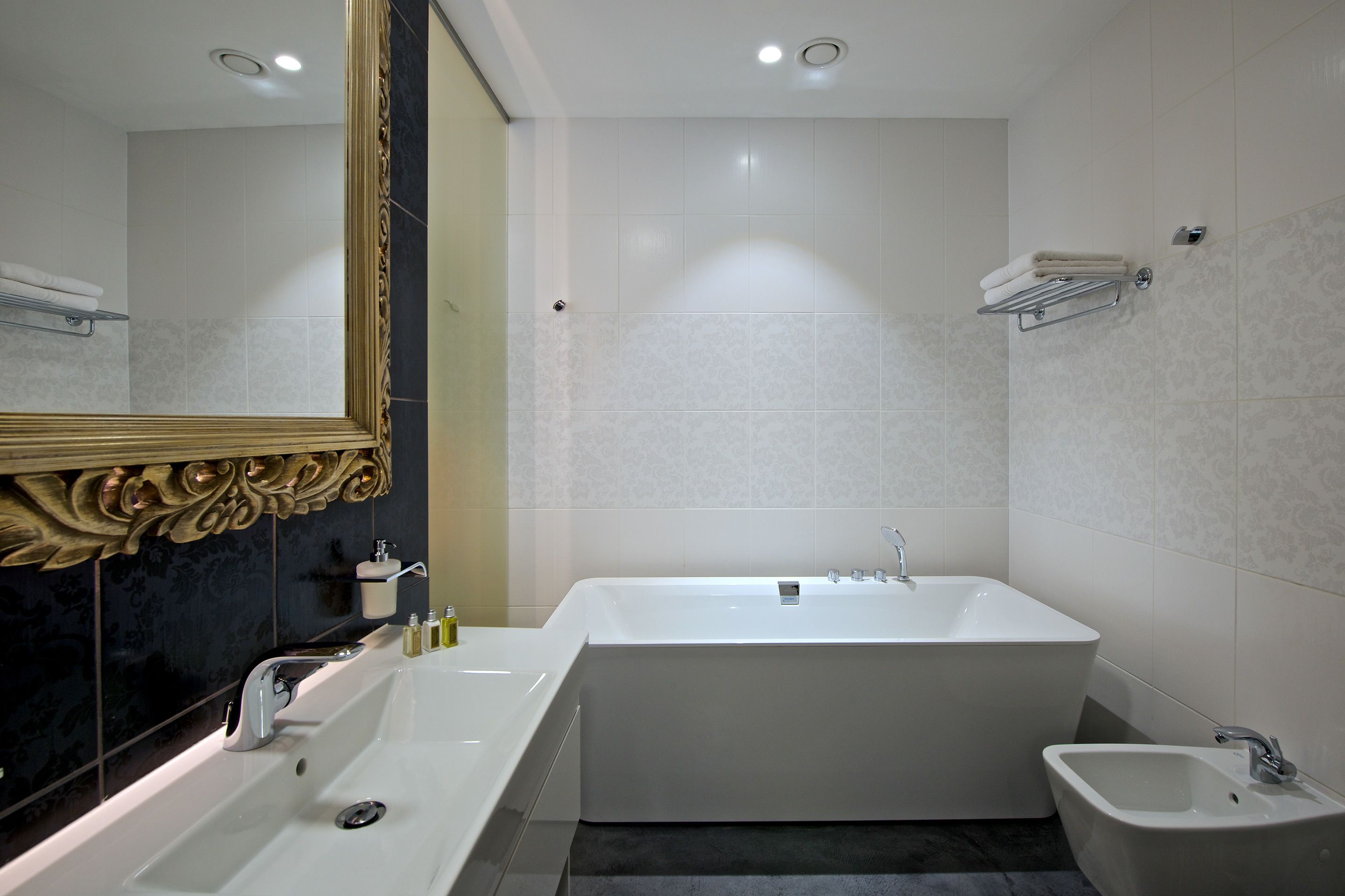 Un baño moderno con una bañera grande, un lavamanos independiente, un bidé y un espejo con un marco decorativo.