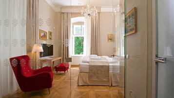 Una habitación de hotel con una cama, un sillón rojo, un televisor y una ventana con cortinas.
