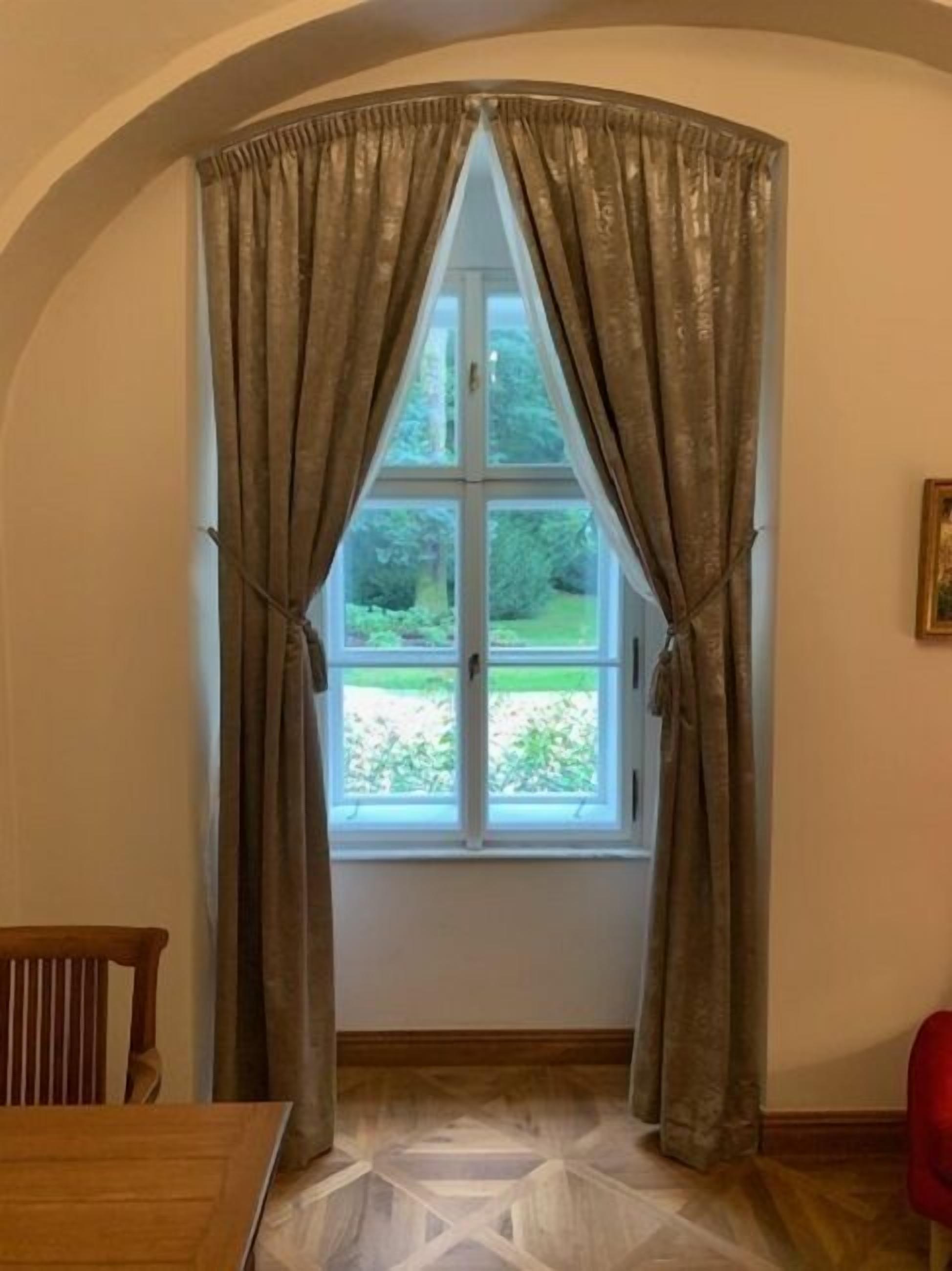 A room with a window framed by a white window frame and brown curtains tied back.