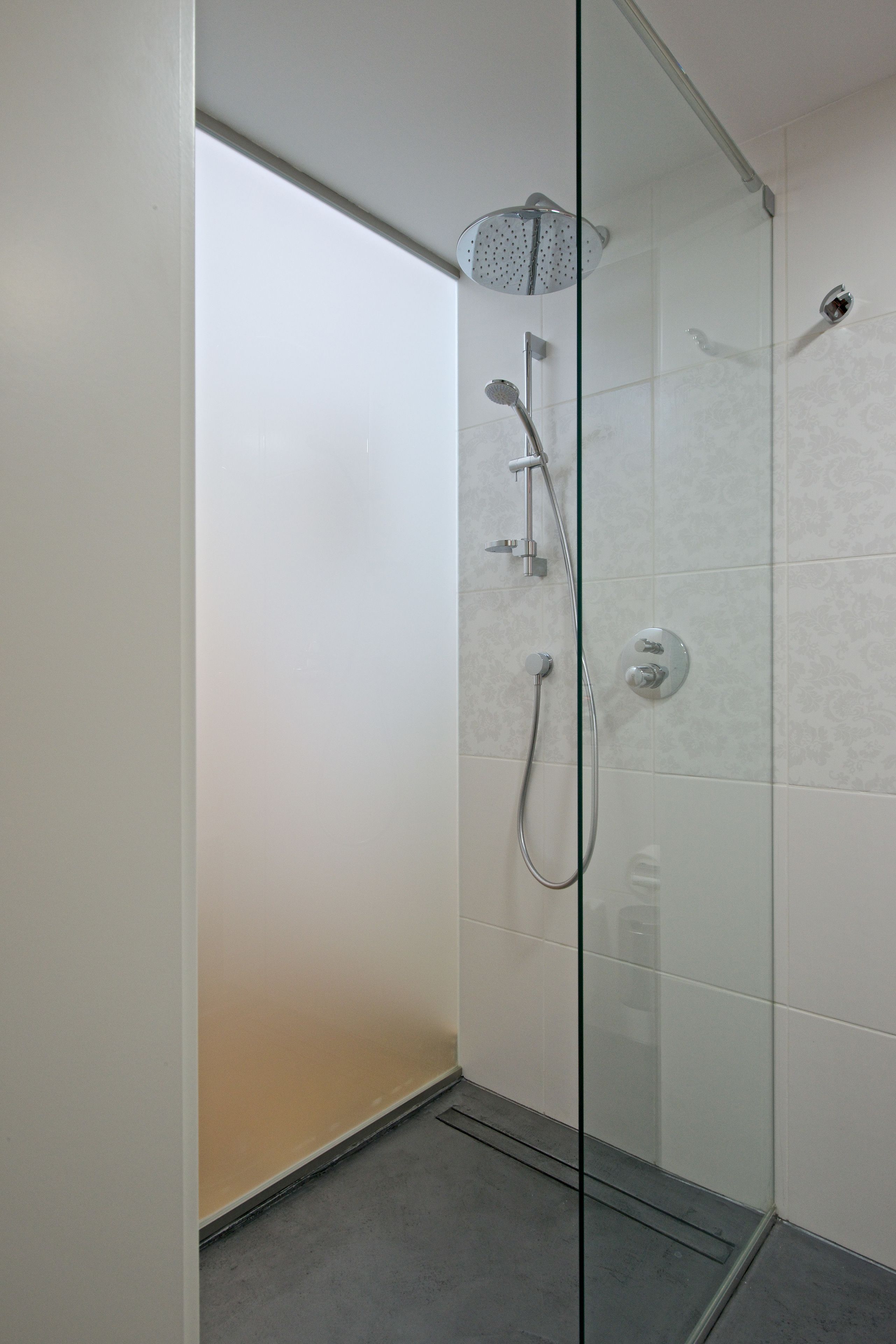 A glass-enclosed shower with a handheld showerhead, a wall-mounted faucet, and a control panel.