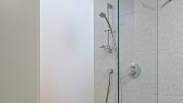 A glass-enclosed shower with a handheld showerhead, a wall-mounted faucet, and a control panel.
