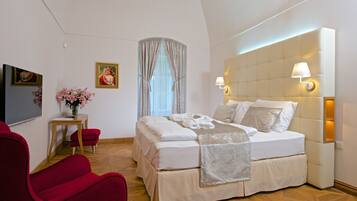 A hotel room with a large bed, a red armchair, a small table with a vase of flowers, and a painting on the wall.