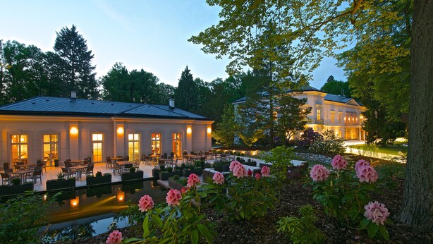 A large building with a covered patio area and a pond with pink flowers in the foreground.