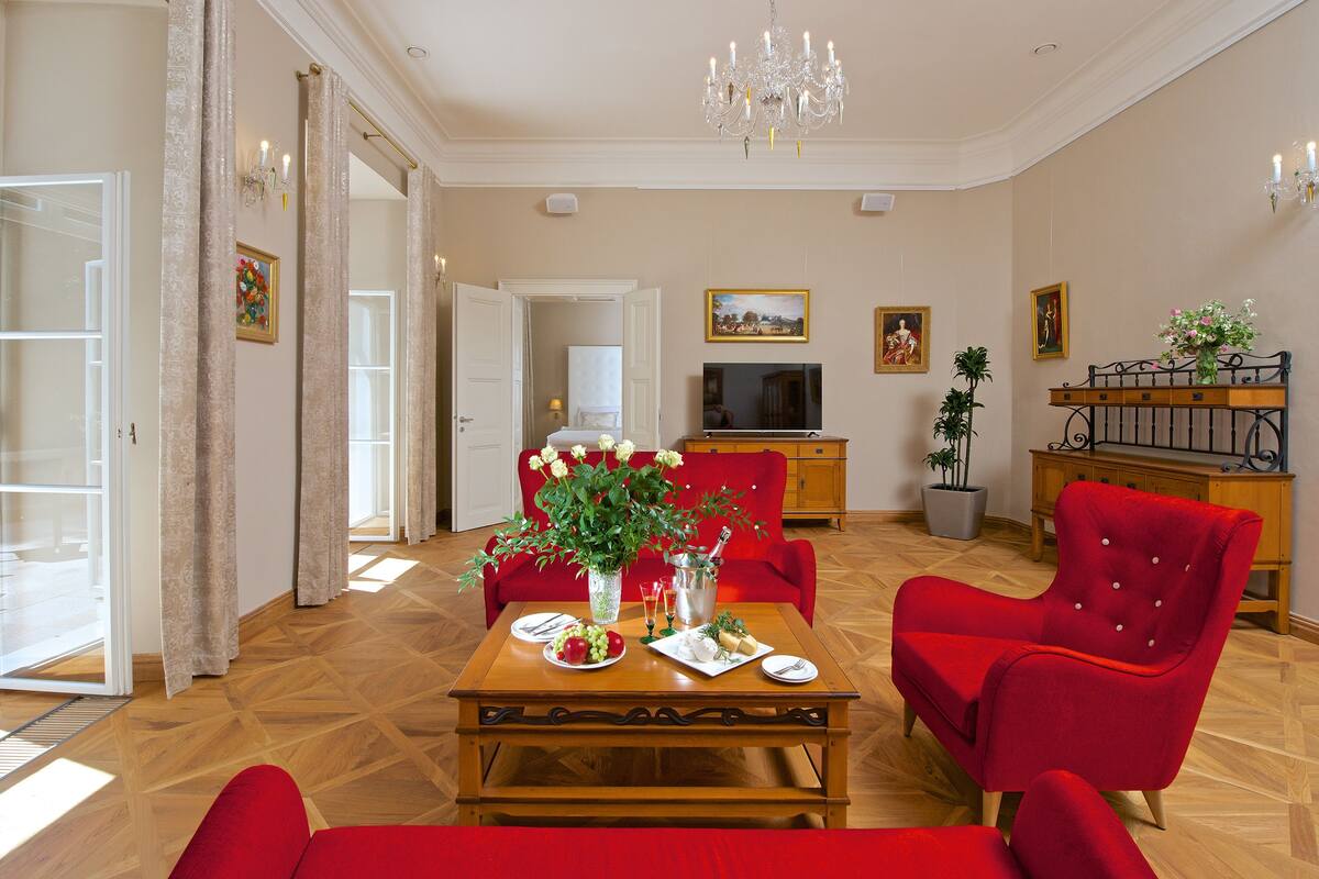 A spacious living room with a wooden coffee table, red armchairs, a television, and a chandelier.