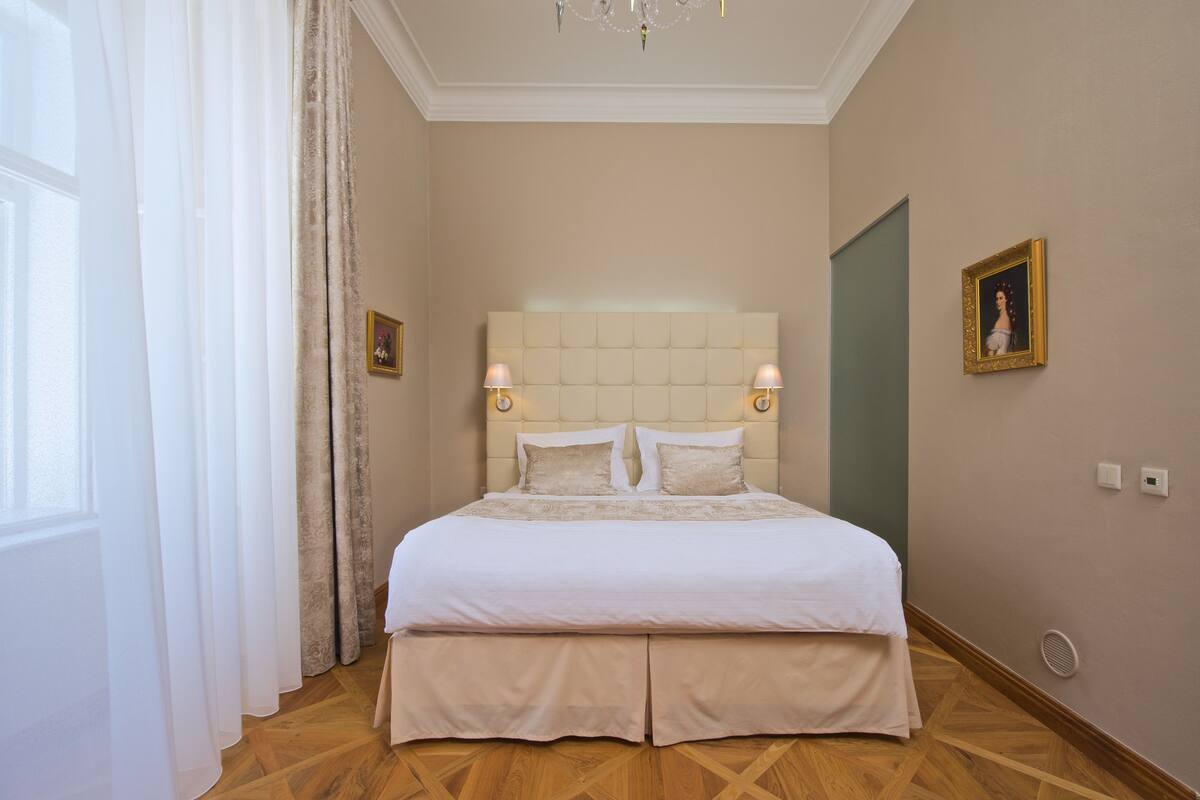 A neatly arranged bedroom with a large bed, two bedside lamps, and a framed picture on the wall.