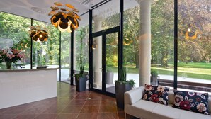 A reception area with a white reception desk, large windows offering a view of greenery, and a white sofa with floral cushions.