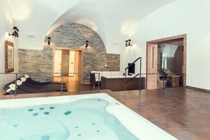 Un área de spa con un jacuzzi, paredes de piedra y un espacio de descanso con chimenea.