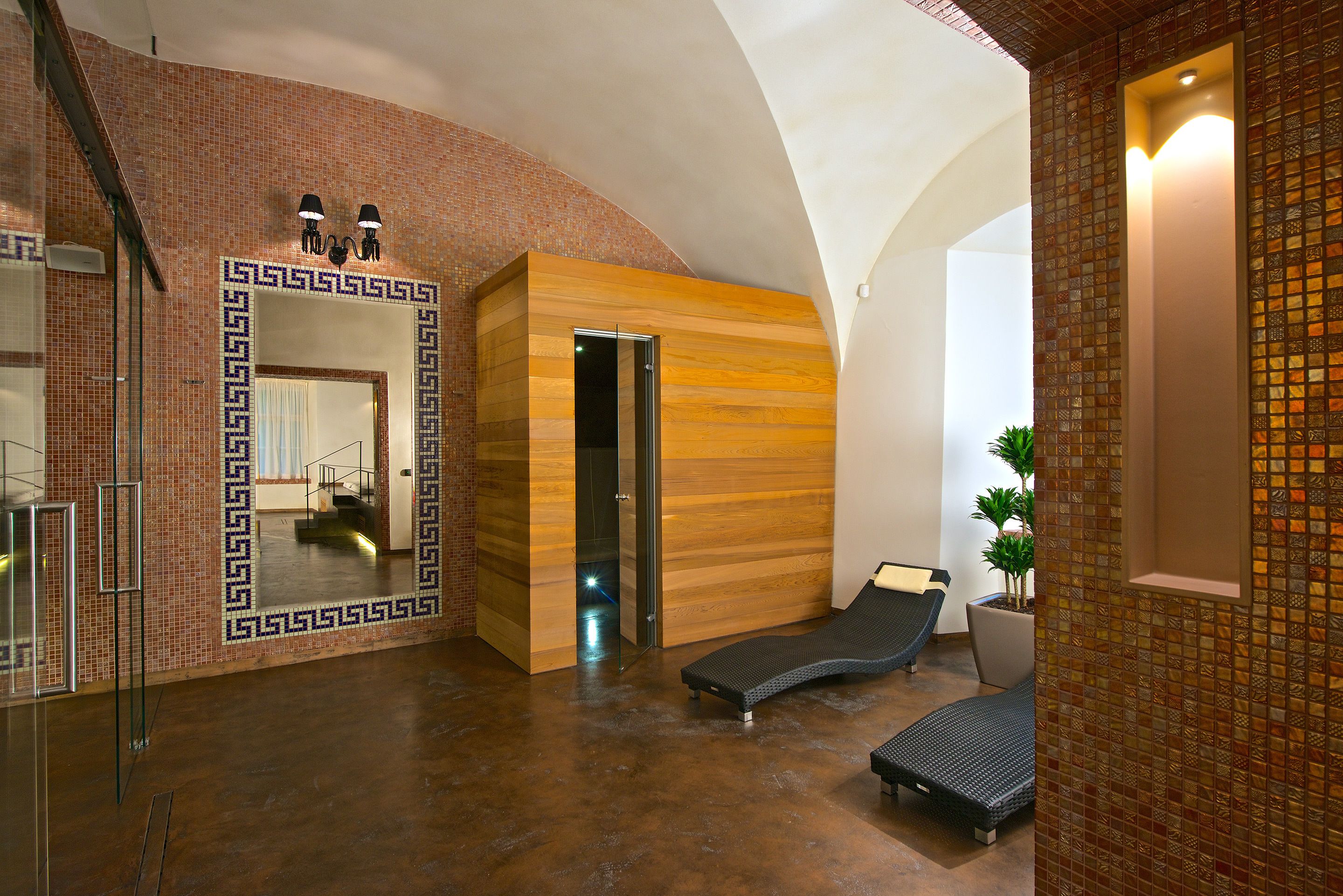 A modern spa area with a wooden wall, a glass door leading to a shower, and two lounge chairs.