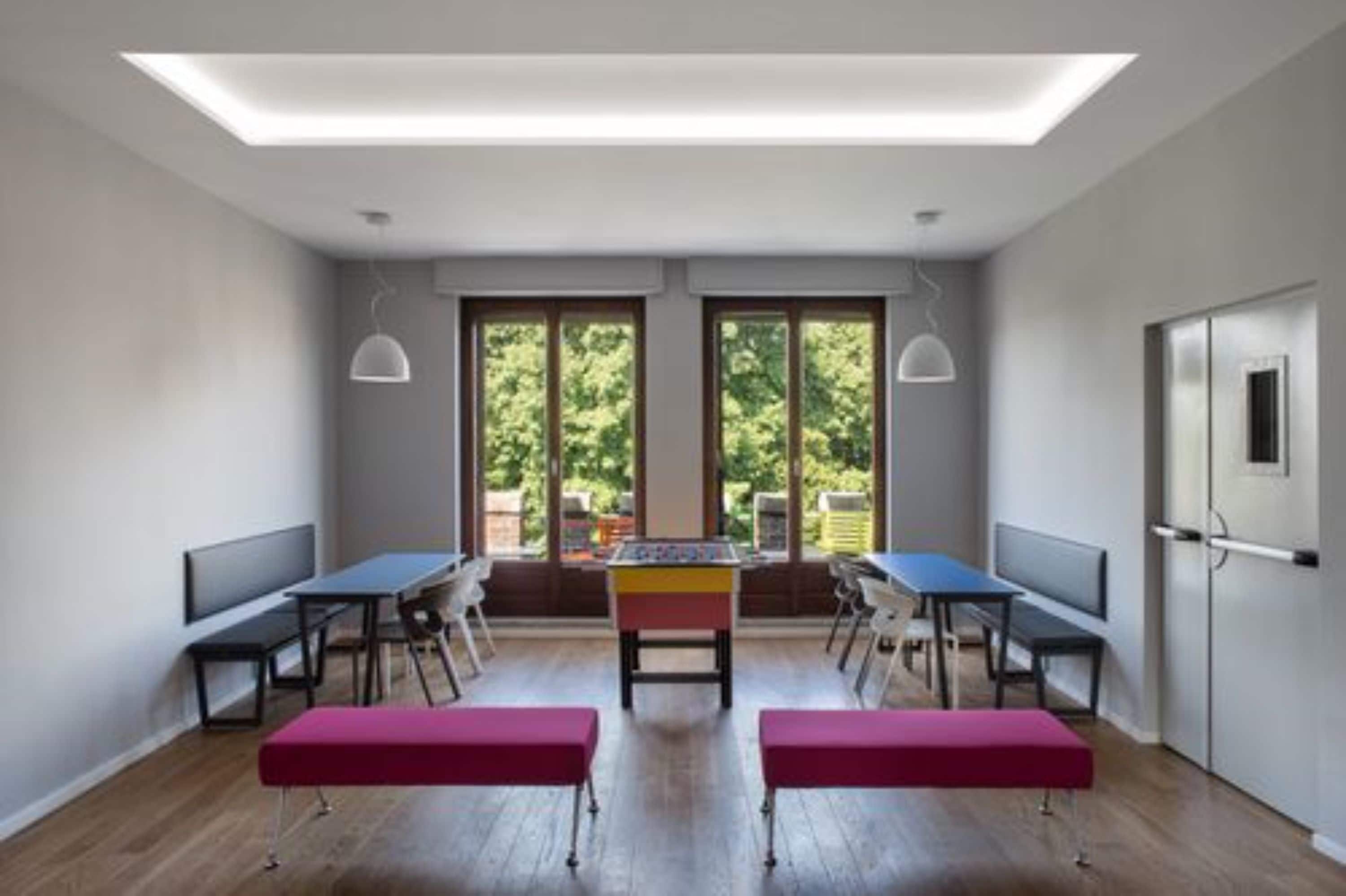 Una habitación moderna con mesa de fútbol de mesa, dos bancos y ventanas amplias con vistas a zonas verdes.