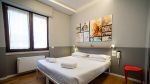Una cama bien hecha con sábanas y toallas blancas, una silla roja y una pared con varias obras de arte.