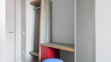 Una stanza con pavimento in legno, un oggetto cilindrico blu, un mobile rosso e grigio e una porta bianca.