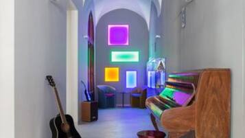 Un pasillo con un techo abovedado imponente, un piano, una guitarra y un jarrón rojo.