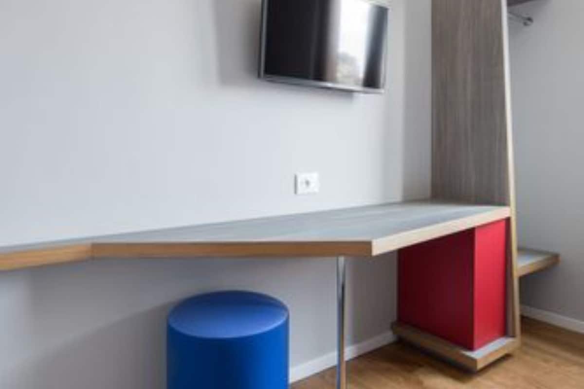 A modern room with a flat-screen TV mounted on the wall, a wooden desk, a blue cylindrical object, and a red cabinet.