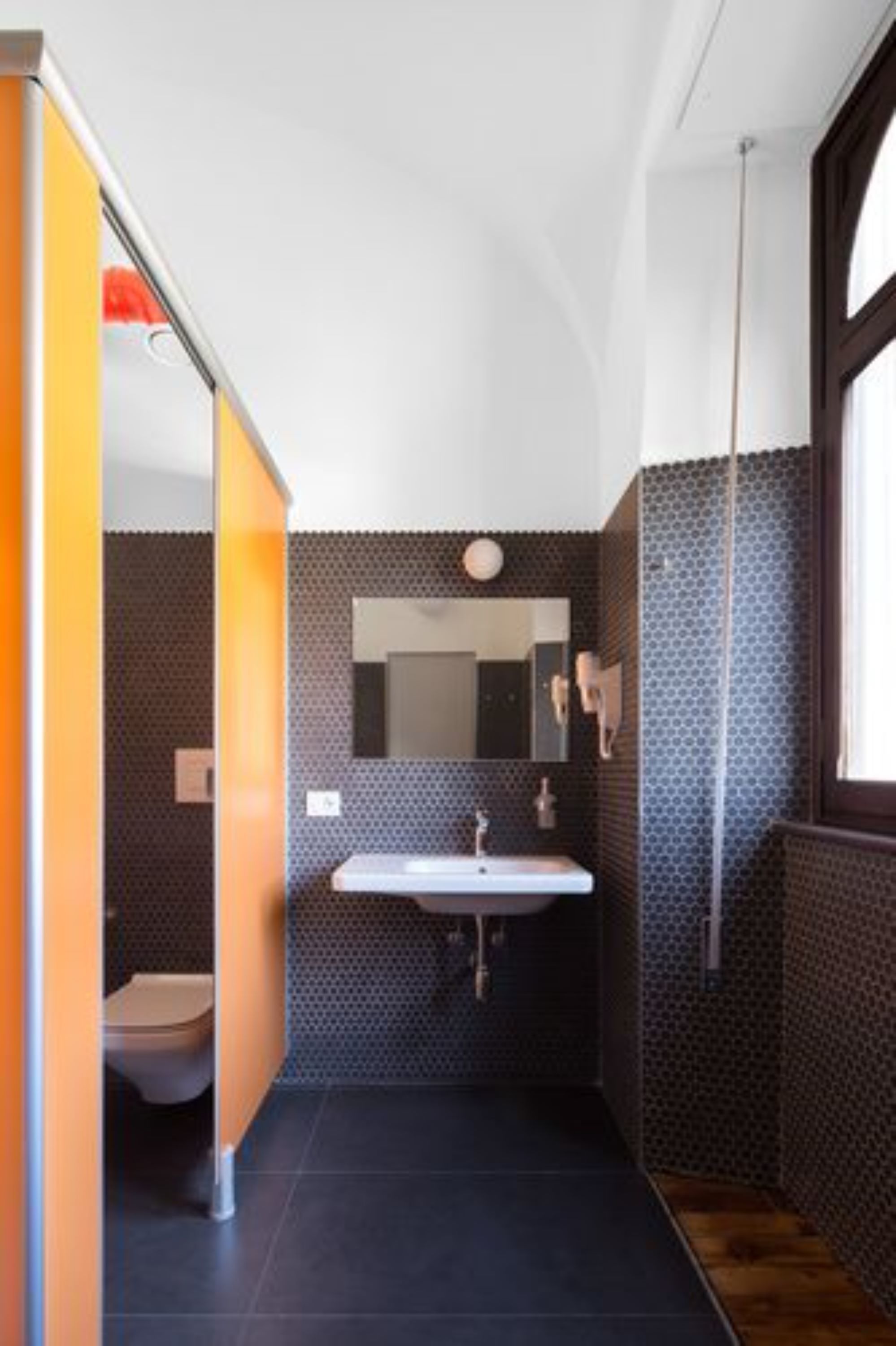 Een moderne badkamer met een donkere betegelde vloer, een witte wastafel en een spiegel erboven.