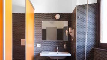 Un bagno moderno con pavimento piastrellato scuro, un lavandino bianco e uno specchio sopra.