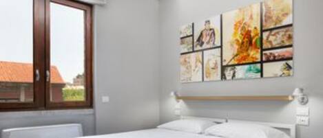 Un dormitorio con una cama grande, una ventana con vistas a edificios y una pared decorada con varias obras de arte.