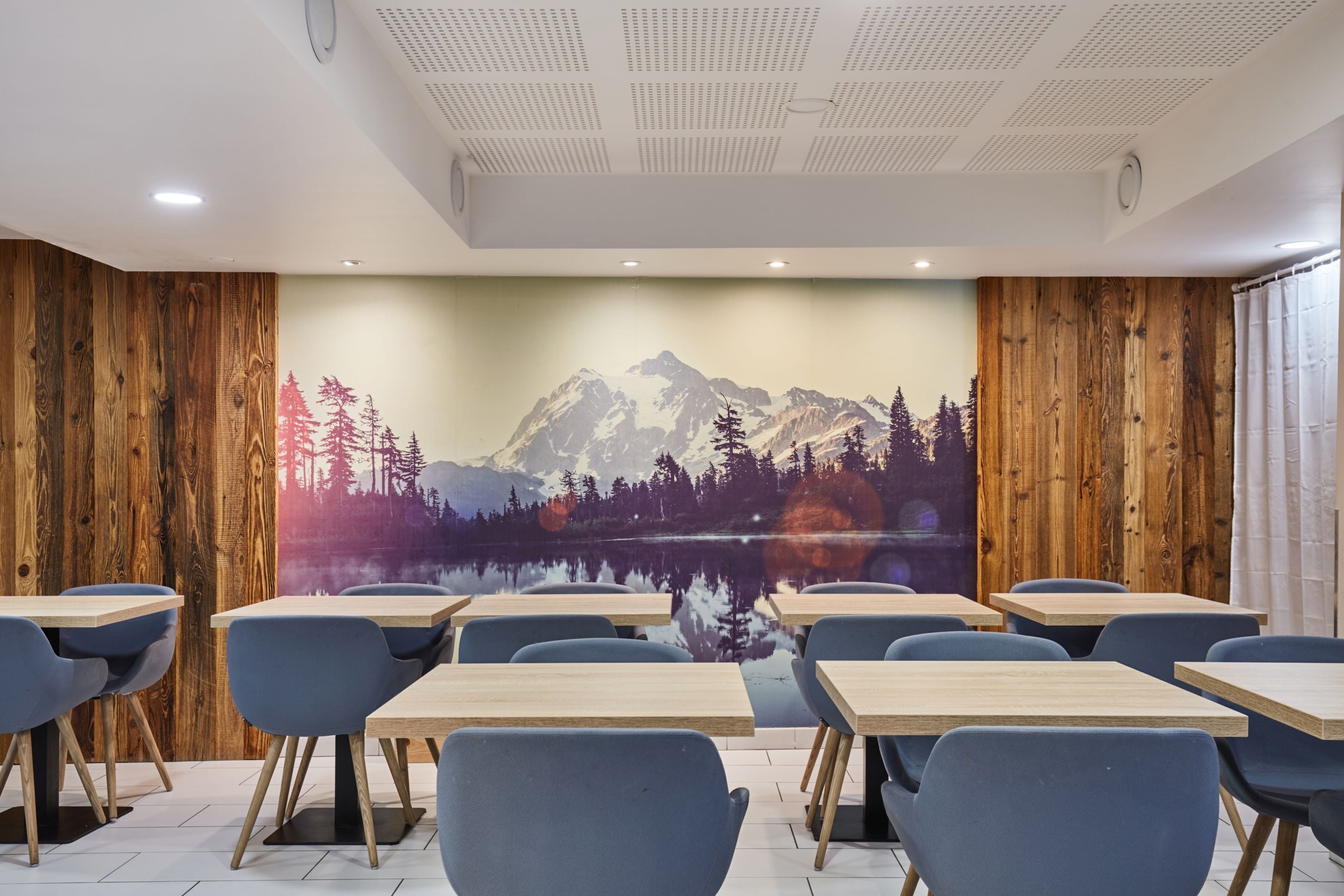 Une salle de conférence aux murs lambrés, ornée d’une fresque représentant un paysage de montagne, et comprenant plusieurs tables et chaises.