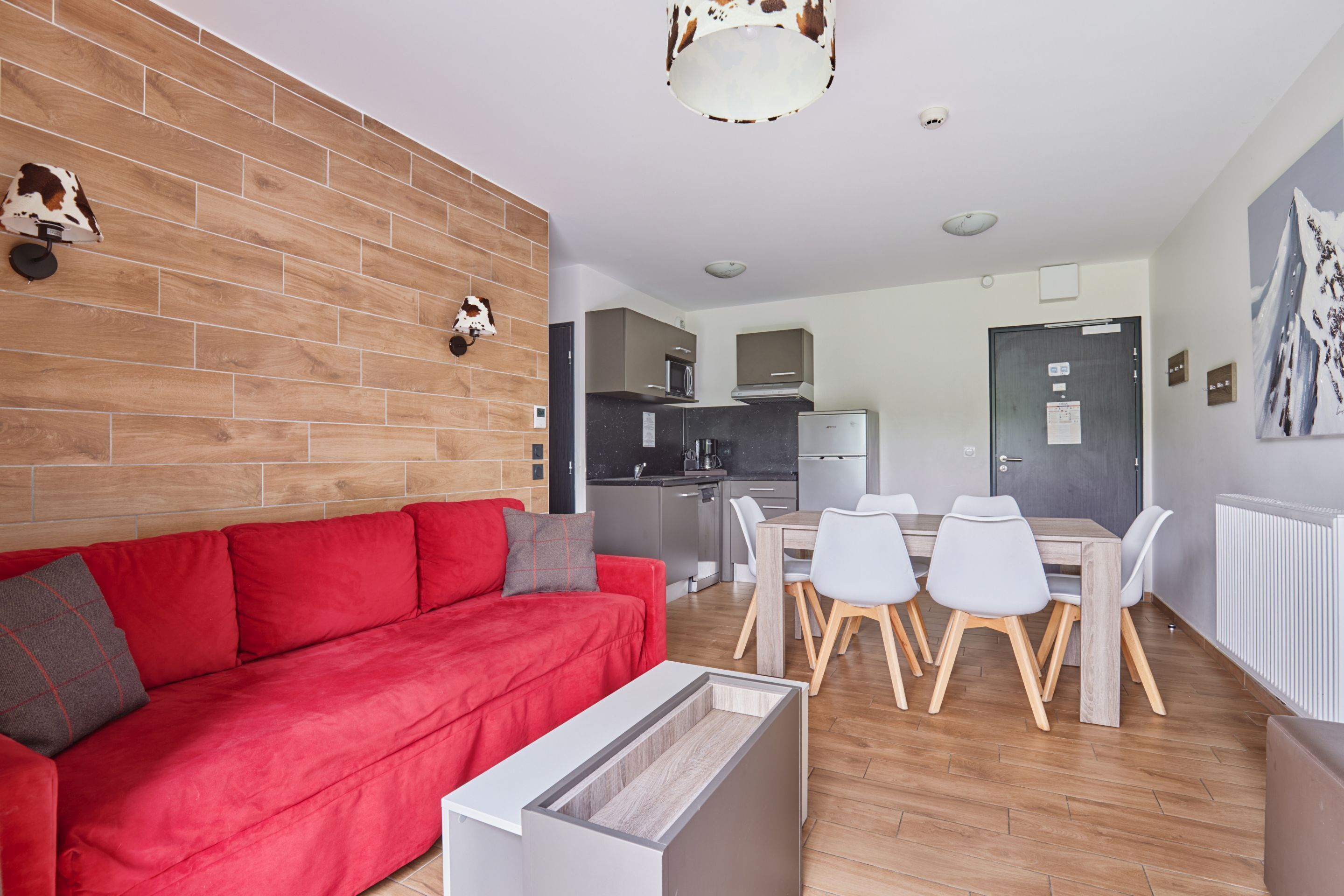 Un salon moderne avec un canapé rouge, une table à manger avec des chaises, un coin cuisine et une décoration murale représentant une tête de vache.