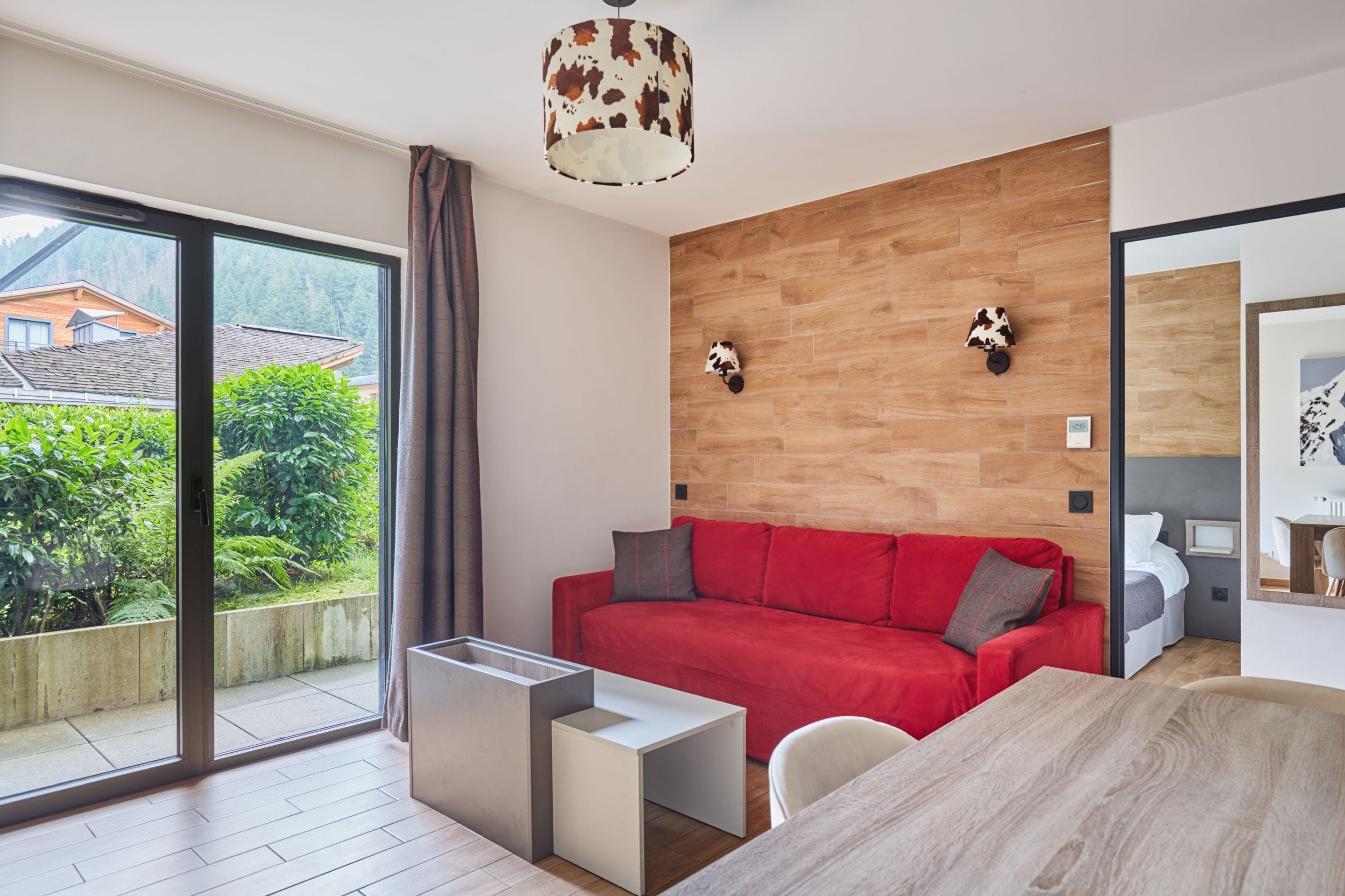 A modern room with a red sofa, a small table, and a view of greenery outside.