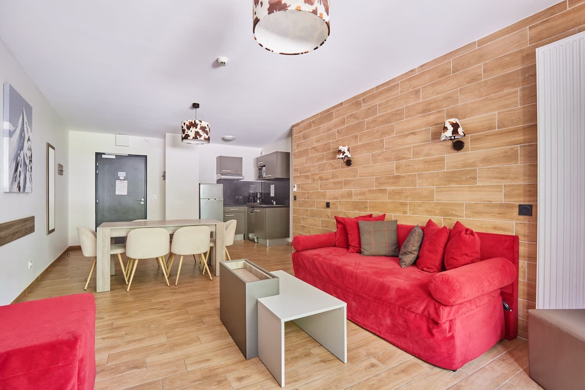 A modern living room with a red sofa, a dining area with a table and chairs, and a kitchen in the background.