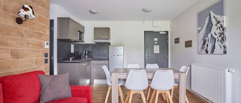 Una cocina moderna con refrigerador, estufa y microondas. Hay un comedor con una mesa y sillas. Se ve un sofá rojo y una almohada gris en primer plano.