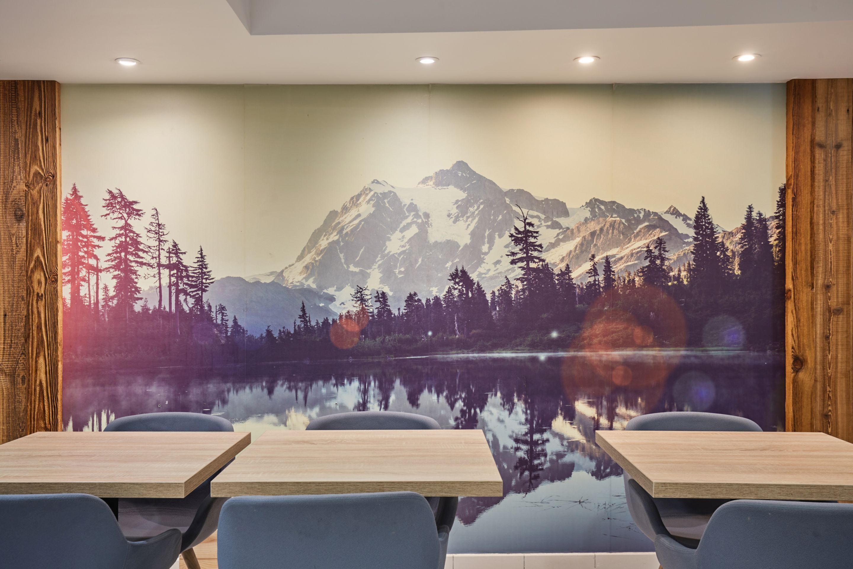 Une salle de conférence ornée d’une fresque représentant un paysage de montagne et un lac. On y trouve quatre tables en bois et six chaises.