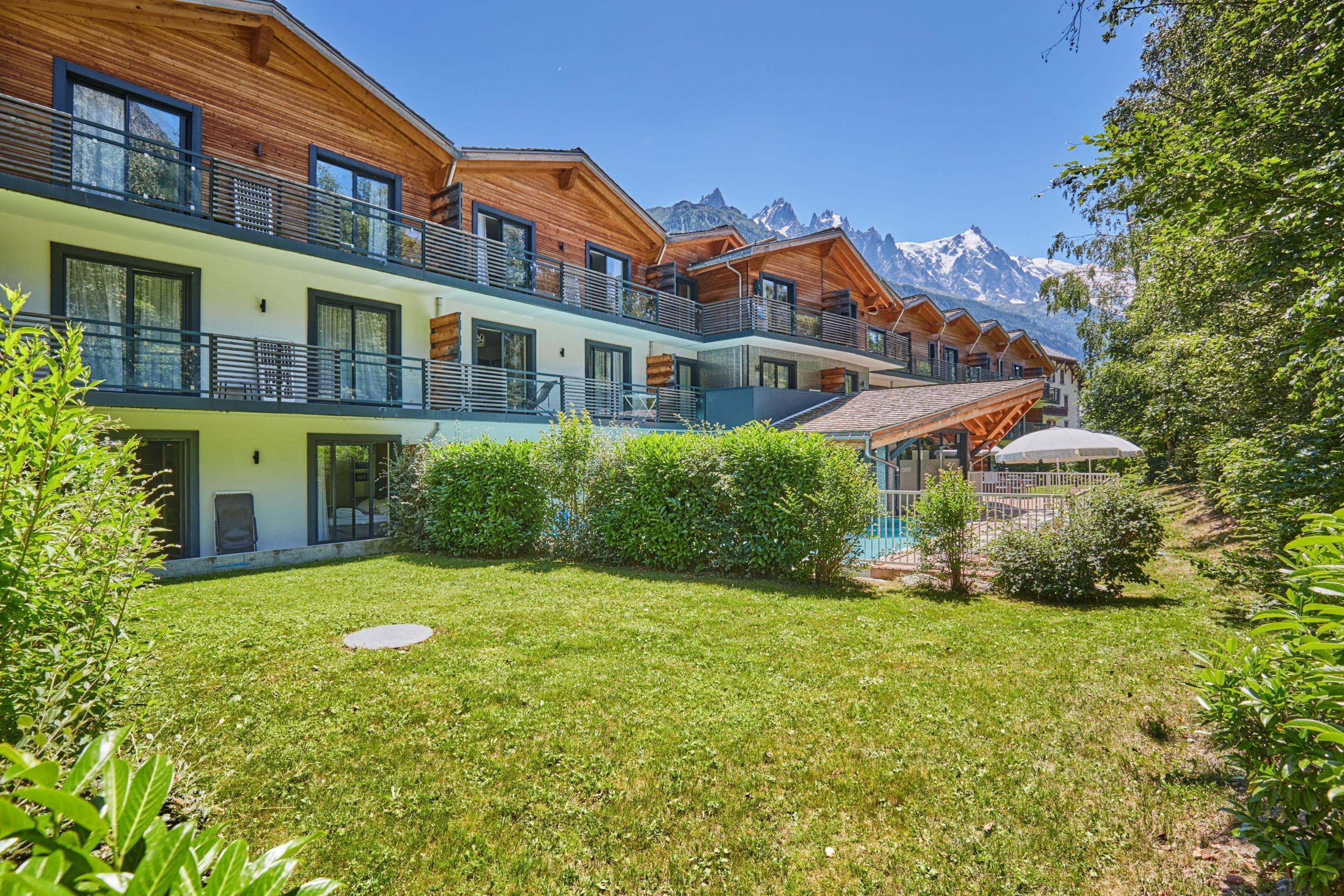 Un hôtel moderne doté de nombreux balcons en bois, d’une pelouse bien entretenue et offrant une vue sur les montagnes.
