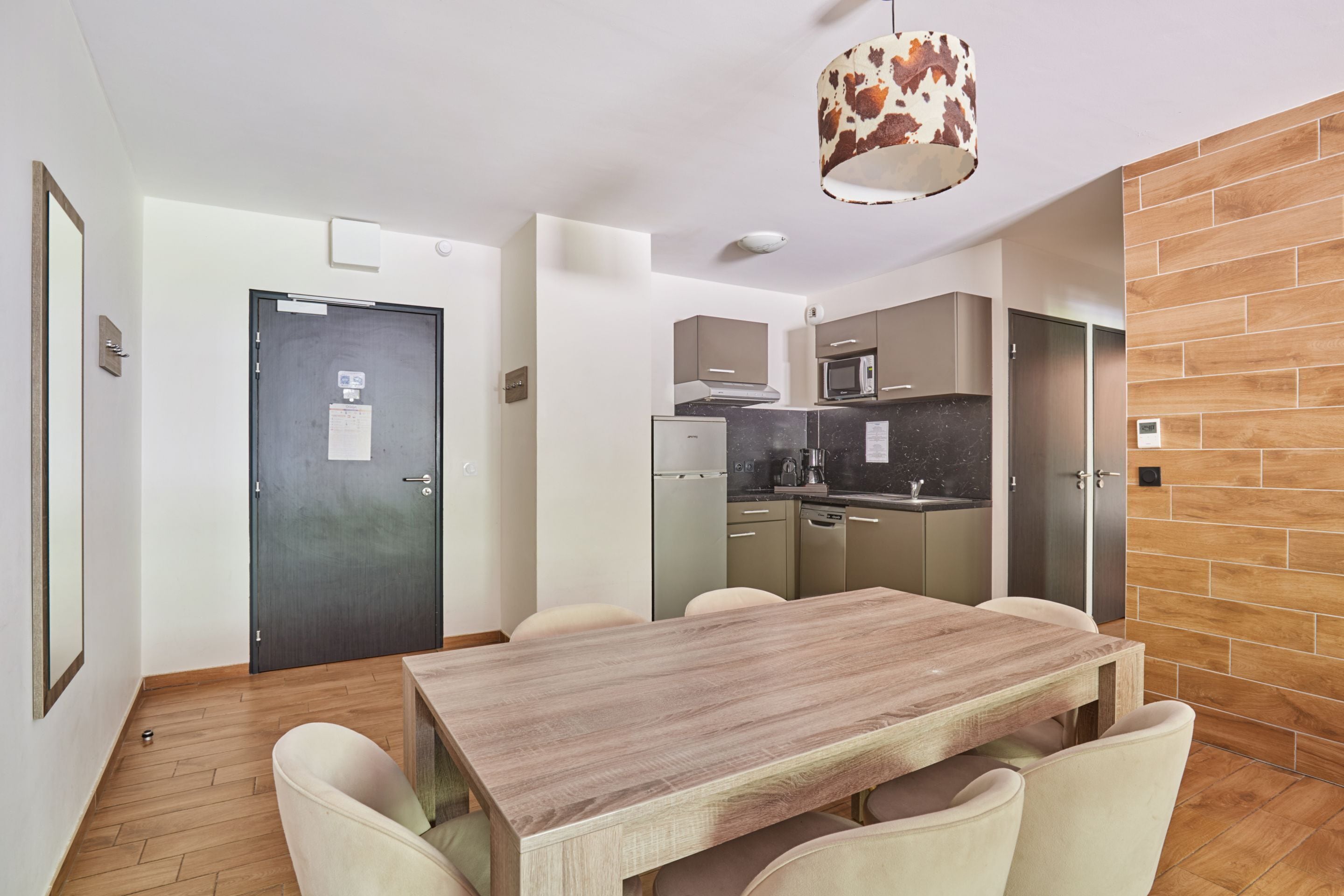 Une cuisine moderne avec une table et des chaises en bois, un luminaire suspendu et un mur d’accent en briques.