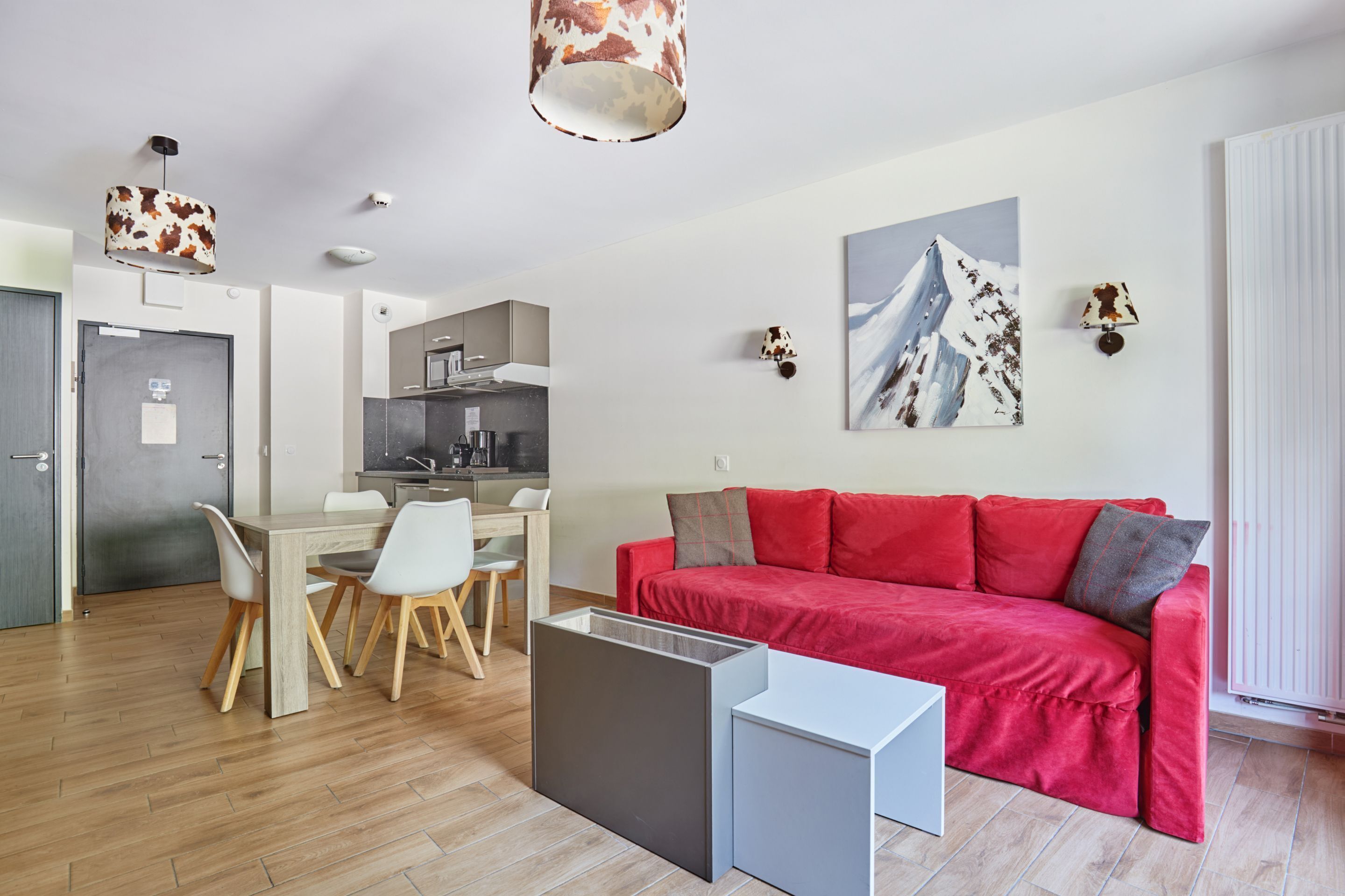 Una sala de estar moderna con un sofá rojo, una mesa de comedor con sillas, una zona de cocina y un ventanal grande.
