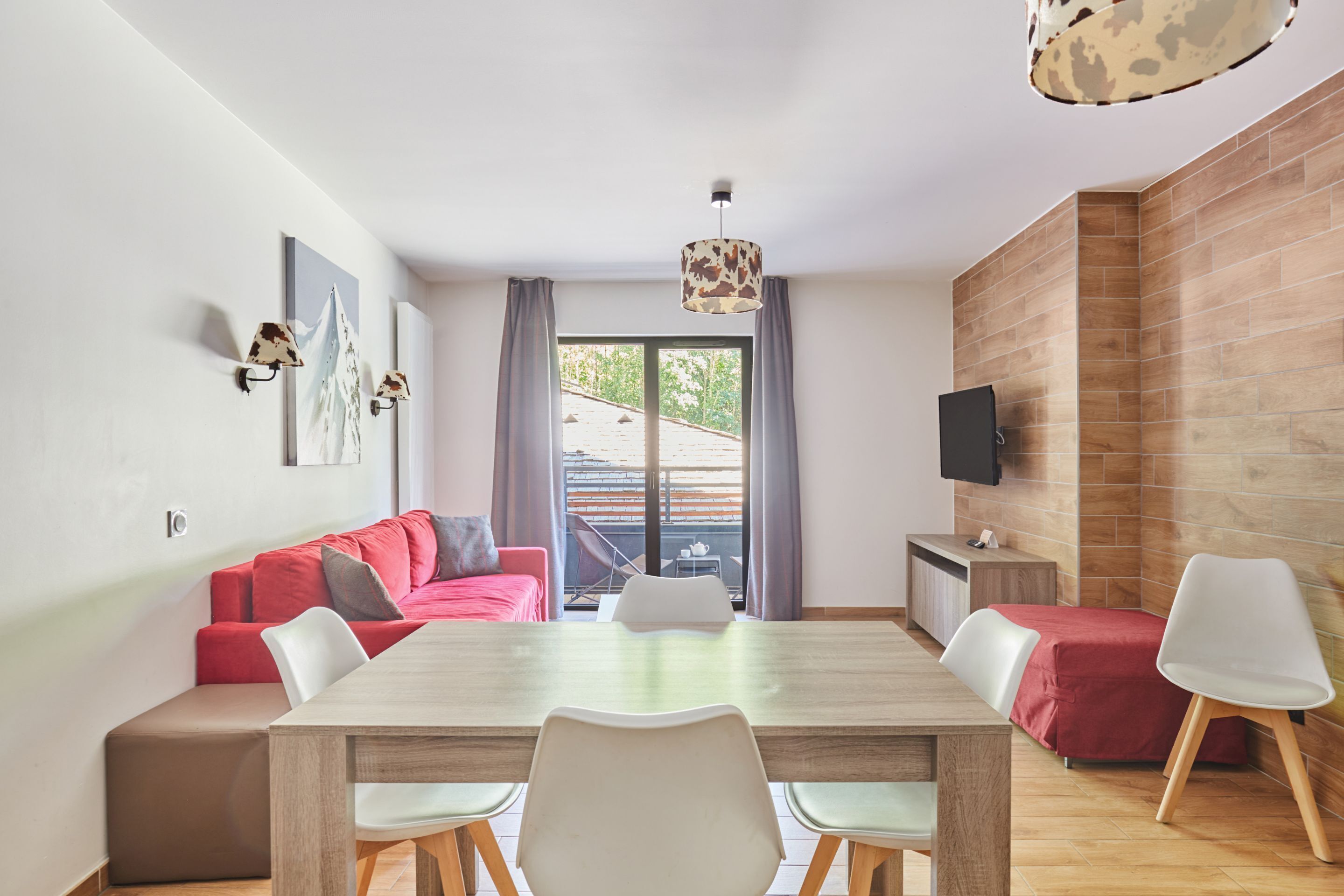 Un salon moderne avec une table à manger en bois, des canapés rouges et blancs, et un téléviseur fixé au mur.