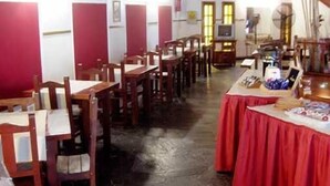A dining area with wooden tables and chairs, a red tablecloth-covered counter with various items, and a television on a stand. - Amparo Hosteria (Neuquén)