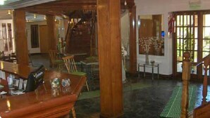 A spacious lobby with wooden flooring, a staircase, and a seating area with tables and chairs. - Amparo Hosteria (Neuquén)