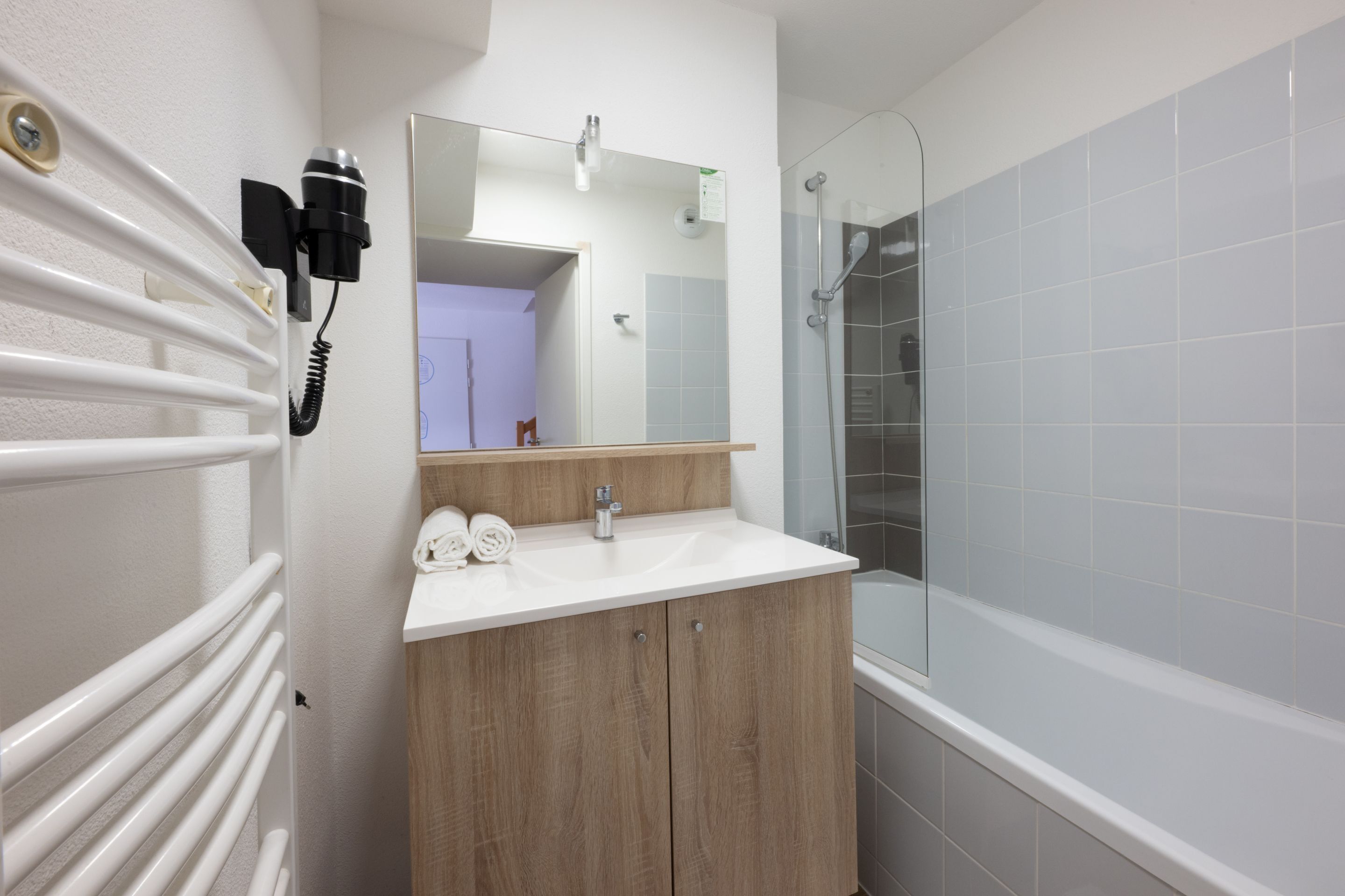A bathroom with a white sink, wooden vanity, a mirror, a shower, and a radiator.