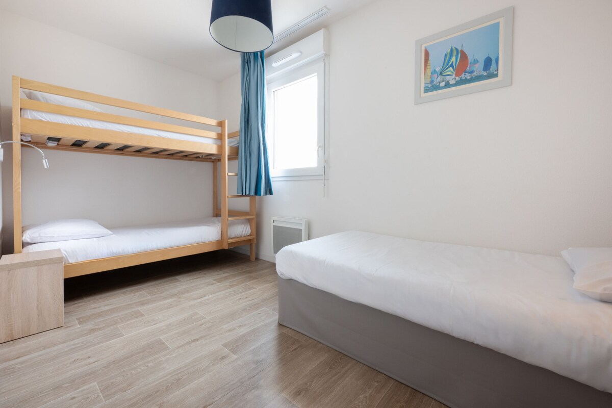Una habitación con una cama individual, una litera, una mesita de noche, una ventana con cortinas y un cuadro en la pared.