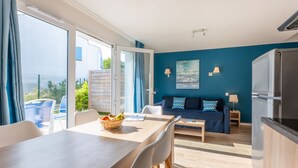 A modern living room with a sofa, dining table, and chairs. There is a balcony with a view of the city. - Résidence Odalys Domaine des Pins - Bois de la Chaise (Noirmoutier-en-l'Ile)