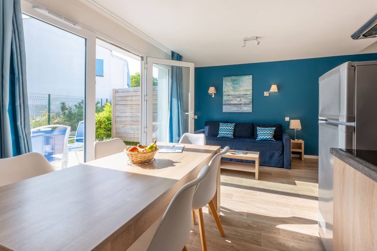 A modern living room with a sofa, dining table, and chairs. There is a balcony with a view of the city.