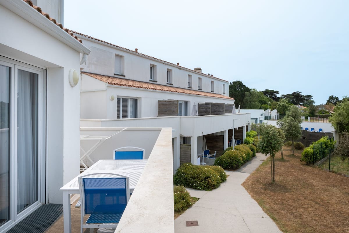 A modern building with a white facade, a tiled roof, and a covered outdoor seating area with blue chairs.