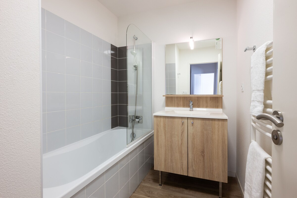 Un baño moderno con ducha de vidrio, tocador de madera con lavamanos y espejo sobre el tocador.