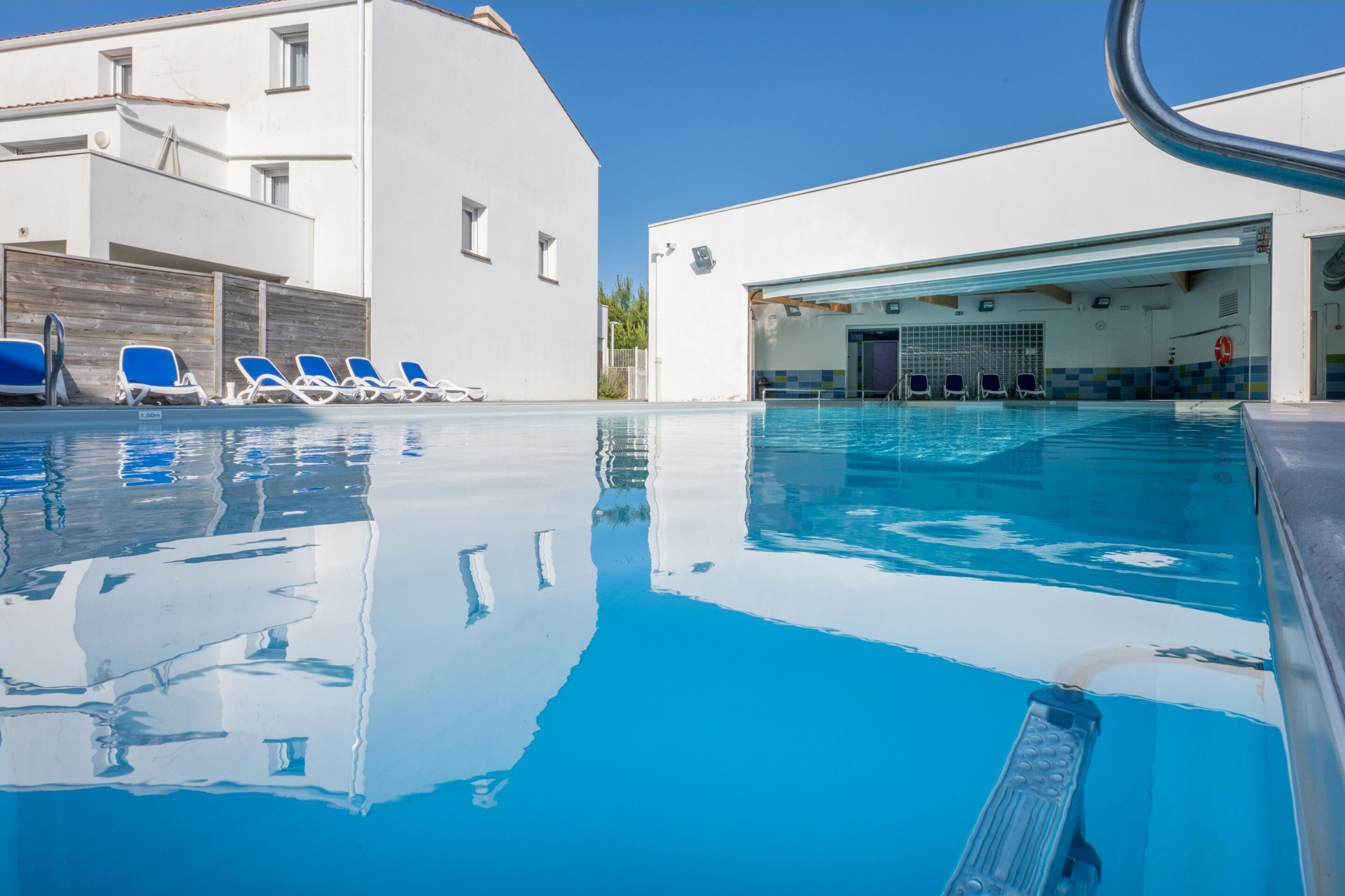Une piscine avec des chaises bleues et un poste de surveillance pour les sauveteurs.