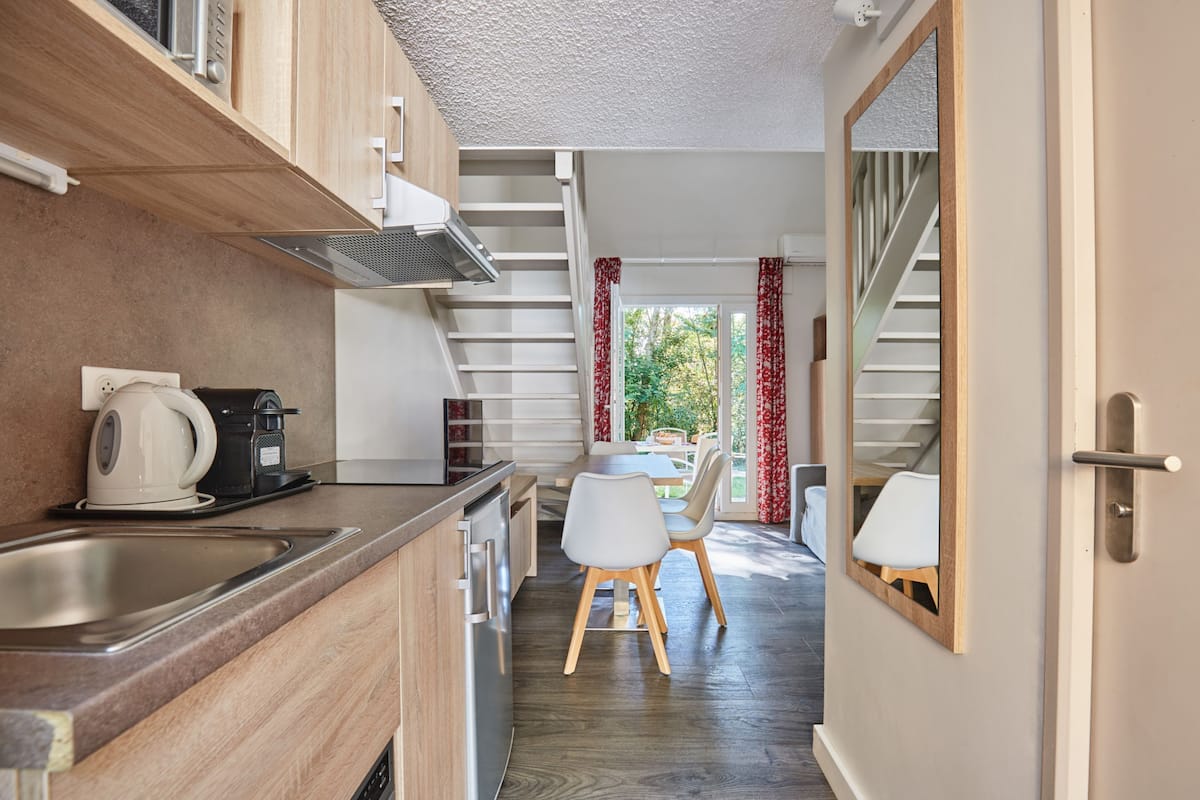 A modern kitchen with a built-in stove, a coffee maker, and a sink. There is a dining area with a table and chairs.