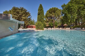 Ein Schwimmbad mit klarem, blauem Wasser, umgeben von Liegestühlen und Sonnenschirmen, mit Bäumen im Hintergrund.