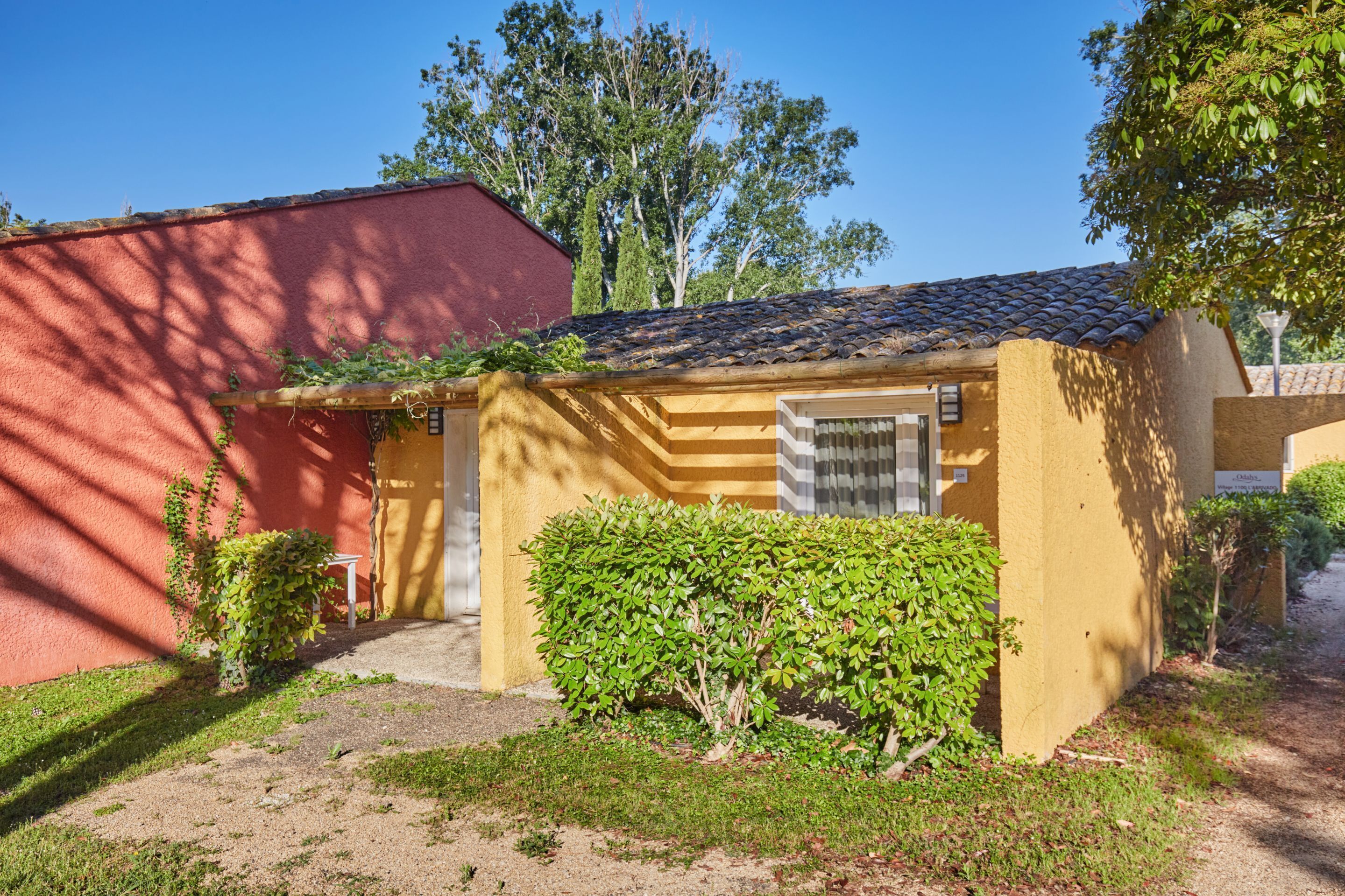 Ein kleines, einstöckiges Gebäude mit Ziegeldach, einer kleinen Veranda und einem gepflegten Garten.