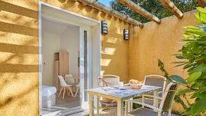 Een terras buiten met een tafel, stoelen, een rieten mand en een witte stoel.