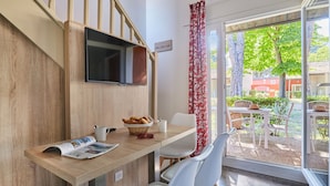 Een eetgedeelte met een houten tafel, witte stoelen, een broodmand en een tijdschrift.