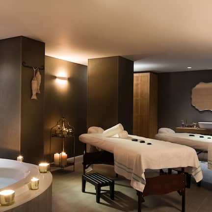 A spa room with two massage tables, a large bathtub, and candles.